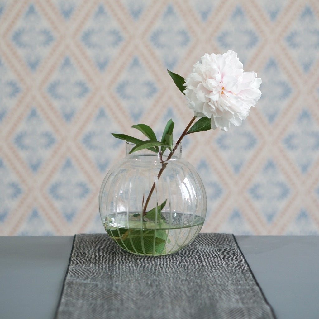 Vase aus Glas auf Tischläufer aus Leinen vor Schwedentapete