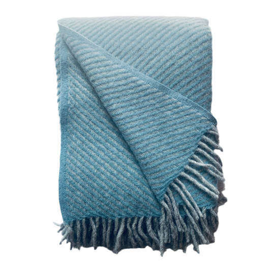 Wolldecke aus Lammwolle Carl blau mit einer aufgeschlagenen Ecke und mit dicken grauen Fransen zusammengefaltet vor neutralem Hintergrund