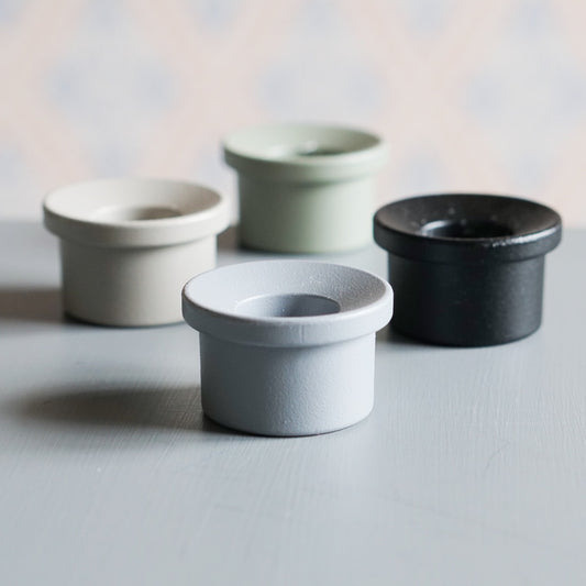 Vier Adapter Kerzenhalter aus Metall in vier Farben auf Tisch vor schwedischer Tapete