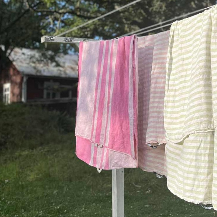 Badetücher Alfons pink und Regnbåge in hellgrün und ziehelrot aus Leinen auf Wäschleine, im Hintergrund Schwedenhaus