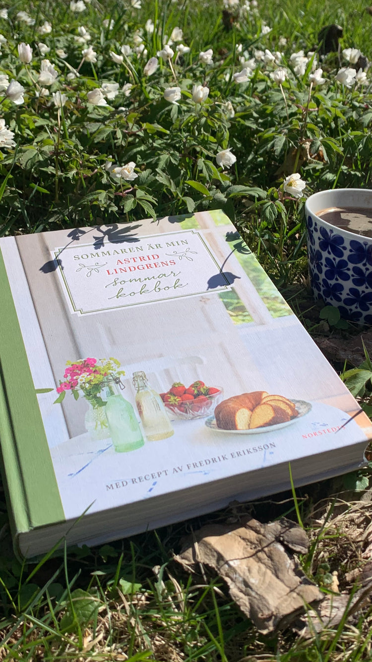 Astrid-Lindgren-Kochbuch und eine Kaffeetasse liegen bzw. stehen in einem Meer aus Buschwindröschen