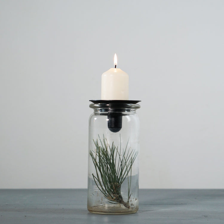 Glas mit Kiefernzweig obenauf der Kerzenhalter Burk in schwarz mit brennender Blockkerze