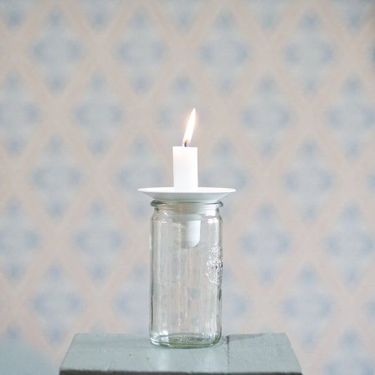 Kerzenhalter Burk aus Metall in weiß mit aufgesteckter brennender Kerze auf einem Glas