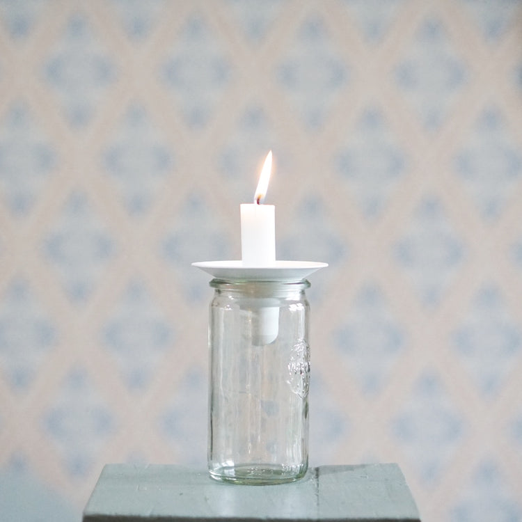 Kerzenhalter Burk aus Metall in weiß mit aufgesteckter brennender Kerze auf einem Glas