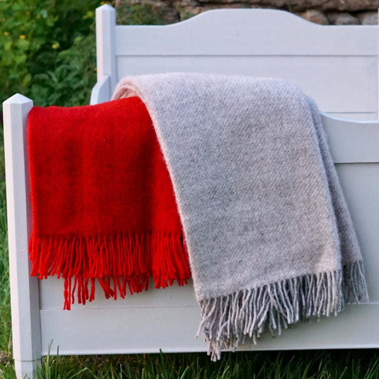 eine rote und eine graue Gotlandwolldecke hängt über dem Fußende eines grauen Holzbettes, das vor einer Steinwand steht