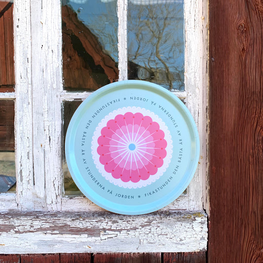 Rundes Tablett „Fikastund“ lehnt außen an der Fensterscheibe eines alten schwedischen Holzhauses mit abgeblätterter Farbe