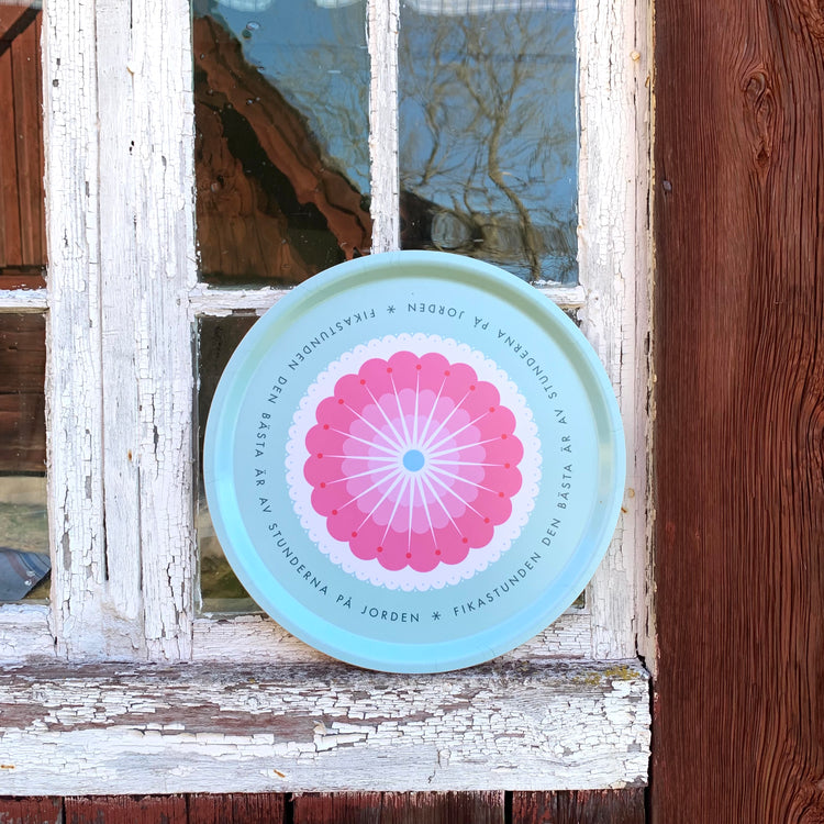 Rundes Tablett „Fikastund“ lehnt außen an der Fensterscheibe eines alten schwedischen Holzhauses mit abgeblätterter Farbe