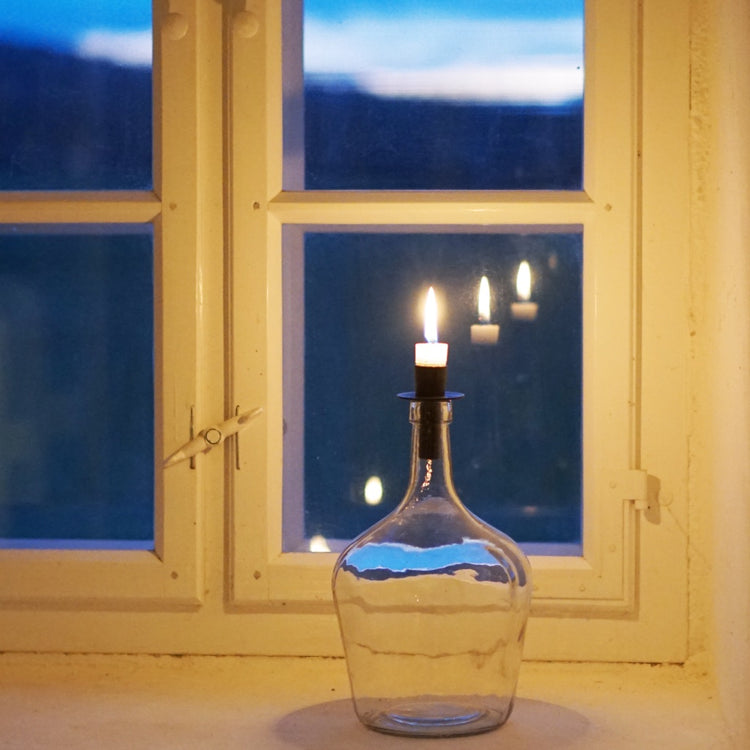 Kerzenhalter Flaska in scharz in einer bauchigen Flasche vor einem Fenster mit Abendhimmel dahinter
