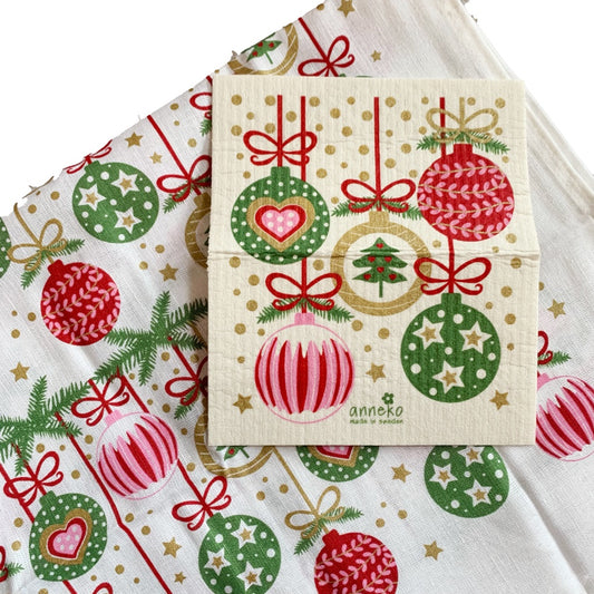 Schwammtuch auf einem Teil des Geschirrhandtuchs liegend, fünf Weihnachtskugeln mit rot/grün/golden Mustern mit roten Aufhängungen sind abgebildet auf dem Schwammtuch. Das gleiche Motiv auf dem Geschirrtuch