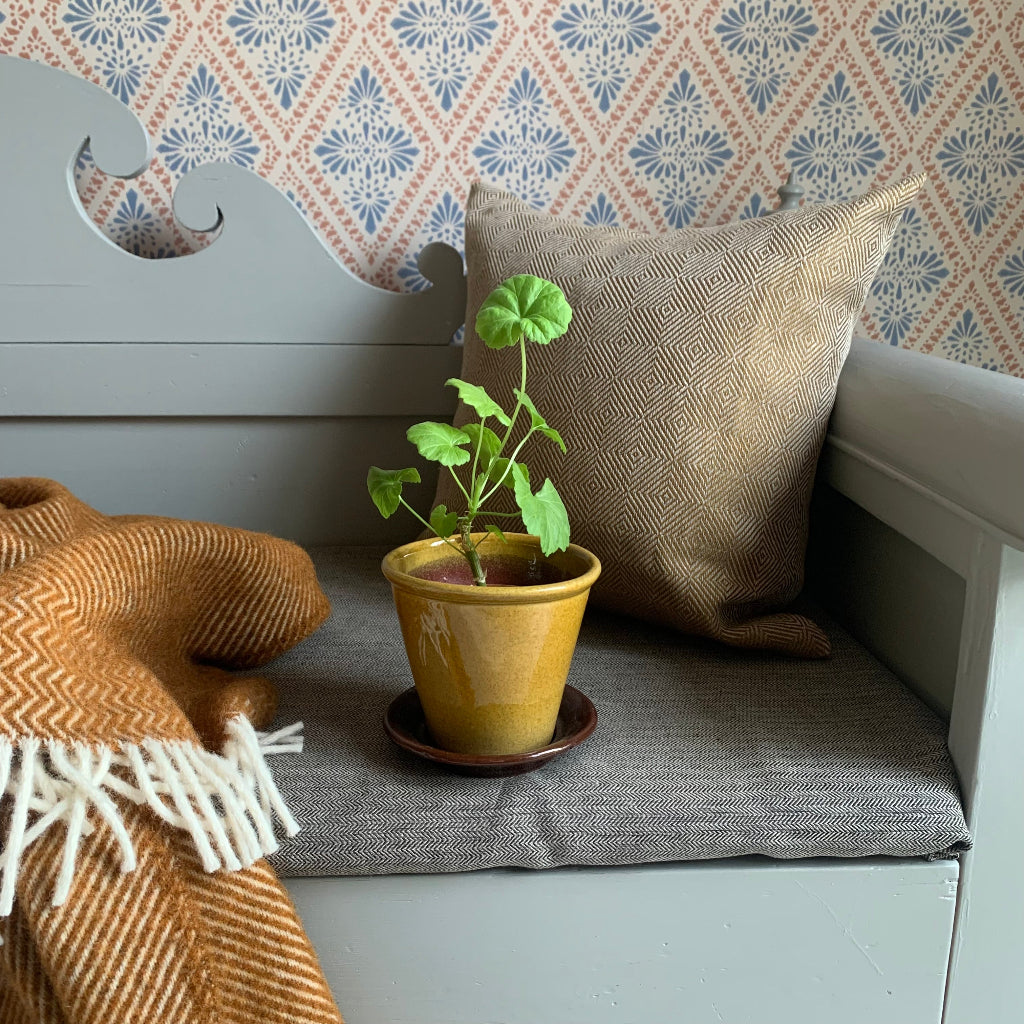 Gränsfors Blumentopf mit Pelargoine auf schwedischem Küchensofa mit Wolldecke