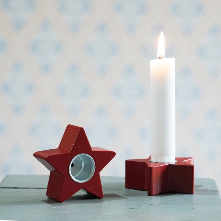zwei Kerzenhalter aus Holz in rot in Form eines Sterns, einer mit brennender Kerze, einer aufrecht stehend, sodass man die Tülle aus metall sehen kann, die vertieft in der Mitte des Sterns ist