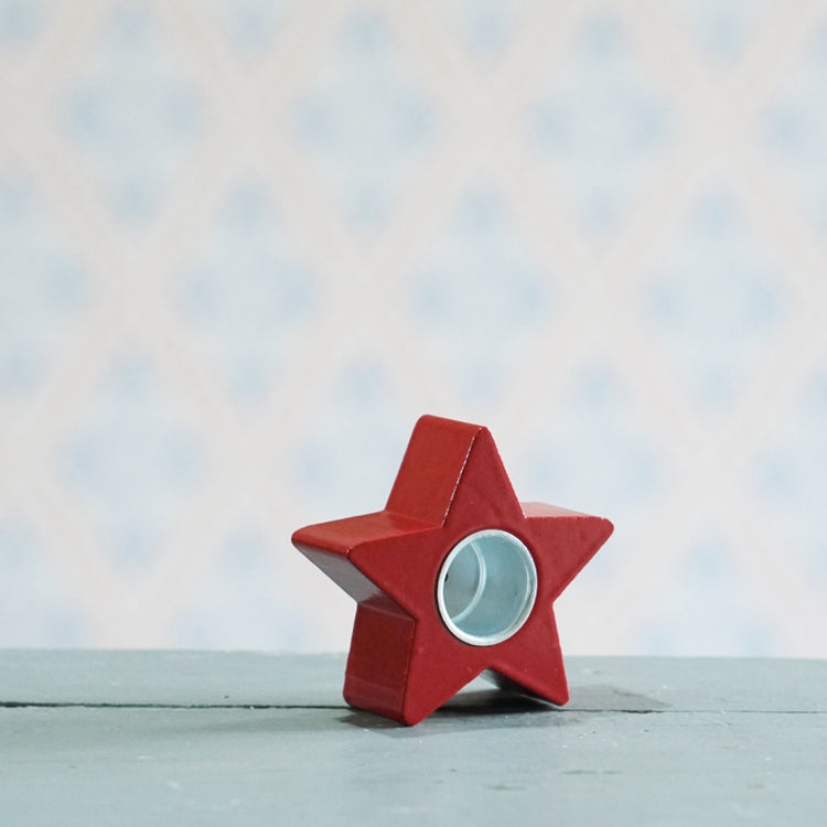 Kerzenhalter aus Holz in rot in Form eines Sterns, aufrecht stehend, sodass man die Tülle aus Metall sehen kann, die vertieft in der Mitte des Sterns ist