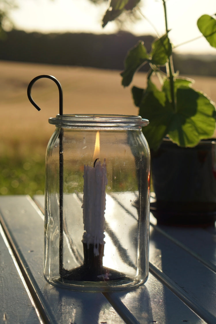Kerzenhaltwr Lykta von Våges in altem Einweckglas auf einem Gartentisch vor einem Feld mit reifem Getreide