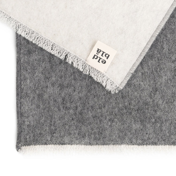 Schal oder Sitzunterlage in grau und weiß mit weißen kurzen zarten Fransen aus Wolle von eldblå