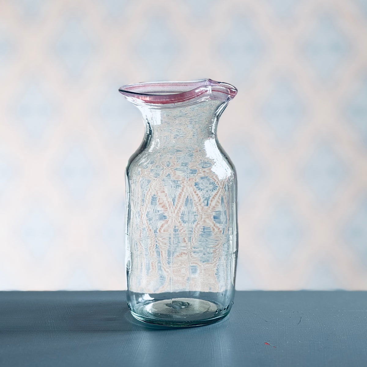 Milchkännchen aus Glas mit rotem Rand vor Schwedentapete