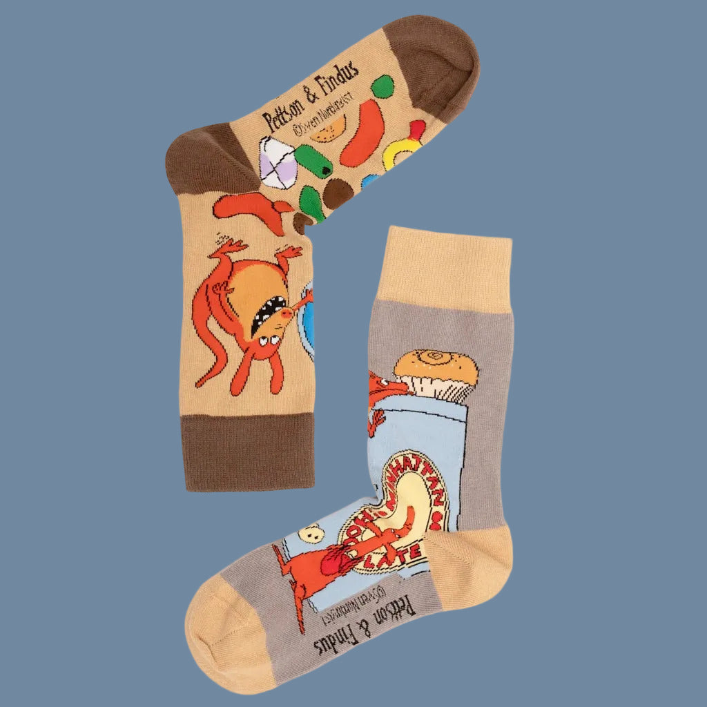 Hellbraune Socke mit brauner Ferse, Spitze, Bündchen und bunten Mucklas samt Süßi, eine graue Socke mit hellbraunem Bündchen, Spitze, Ferse und Mucklas mit Pilzen
