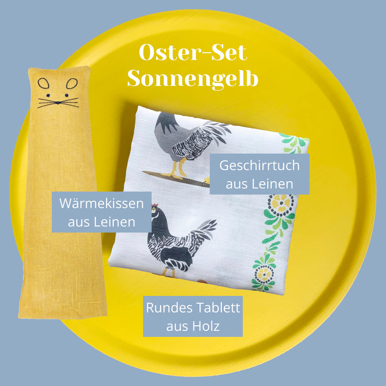 Wärmekissen in dunkelgelb und Geschirrtuch mit Hühnern auf gelbem, rundem Tablett mit Angaben zum Set