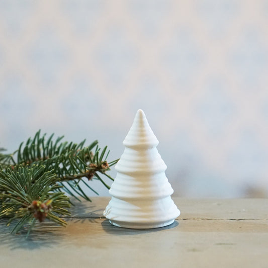 kleiner weißer Tannenbaum aus unglasierter Keramik neben einem Tannewzweig auf Tisch stehend