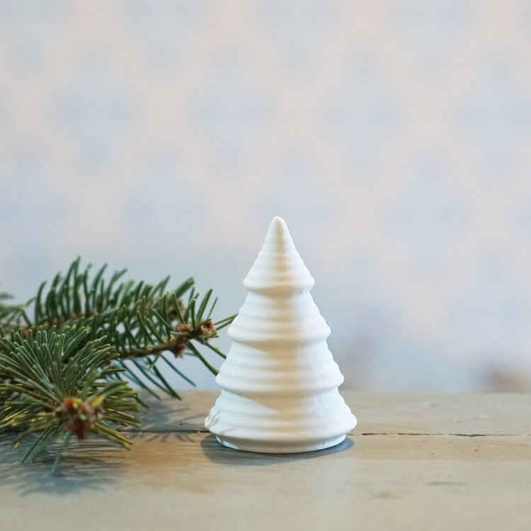 kleiner weißer Tannenbaum aus unglasierter Keramik neben einem Tannewzweig auf Tisch stehend
