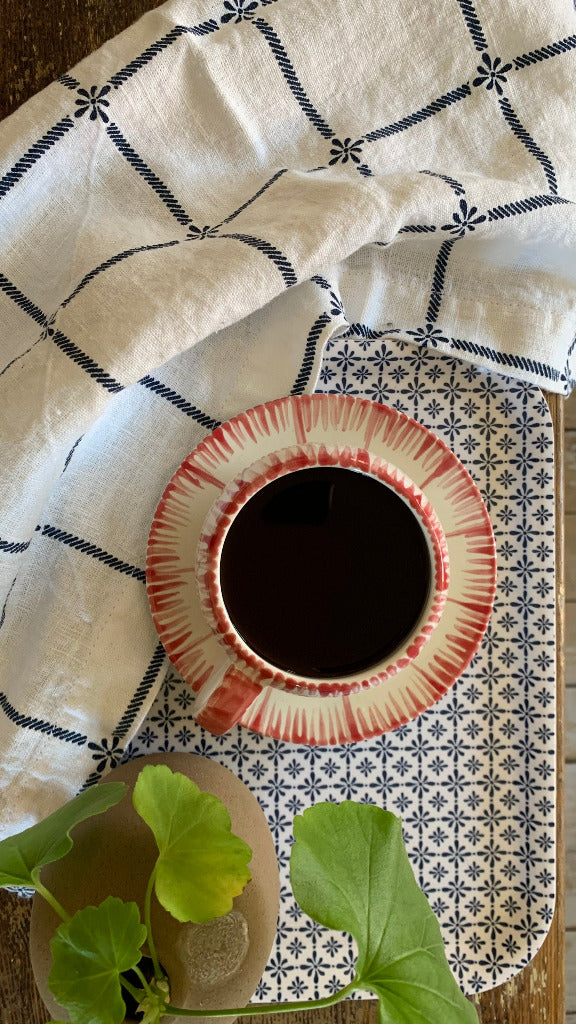 Tasse mit rotem Muster auf Tablett Destiny dazu ein Geschirrtuch Classic und eine Pelargonie