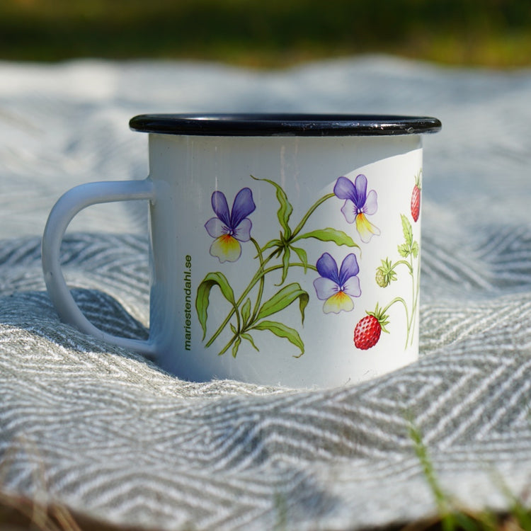 Emailletasse mit Sommerblumen auf Leinenläufer beim Picknick