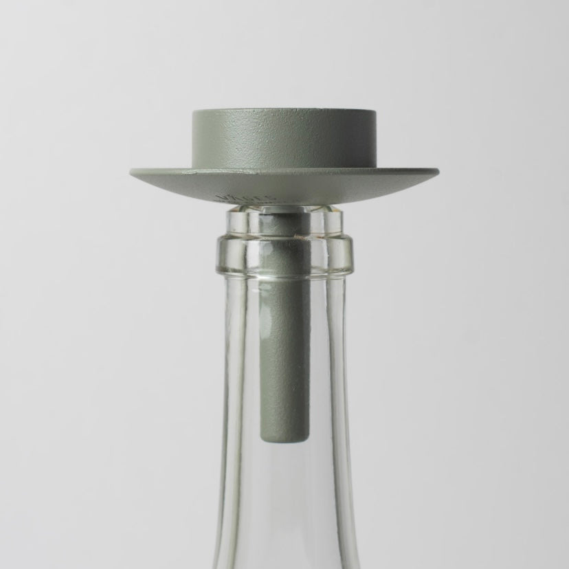Teelichthalter aus Metall wiesengrün auf weißer Glasflasche