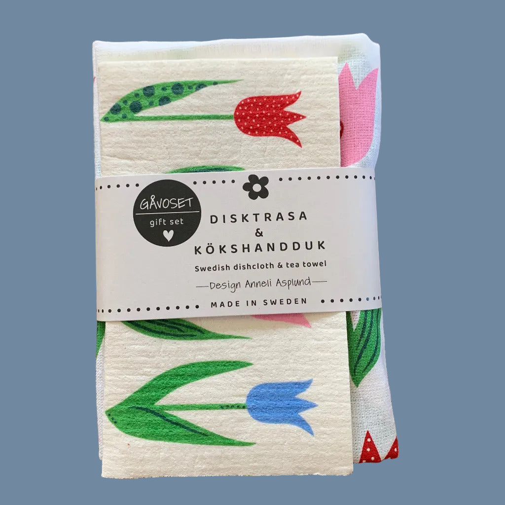 Geschenkset Geschirrtuch und Schwedisches Spültuch mit Tulpen zusammengefaltet mit Banderole vor mysblauem Hintergrund