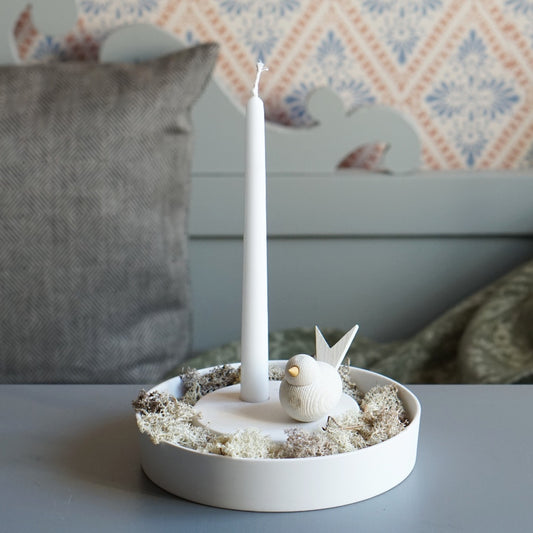 Kerzenhalter in weißer Keramik mit Weißmoos im vertieften Rand, obenauf eine weiße Kerze und ein Holzvogel in weiß