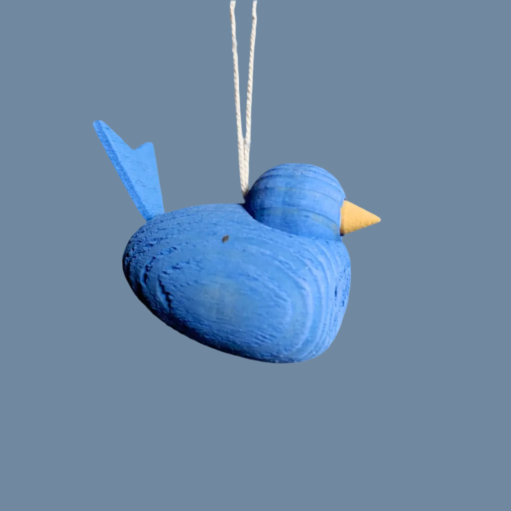 kleiner blauer Holzvogel an weißem Band vor mysblauem Hintergrund