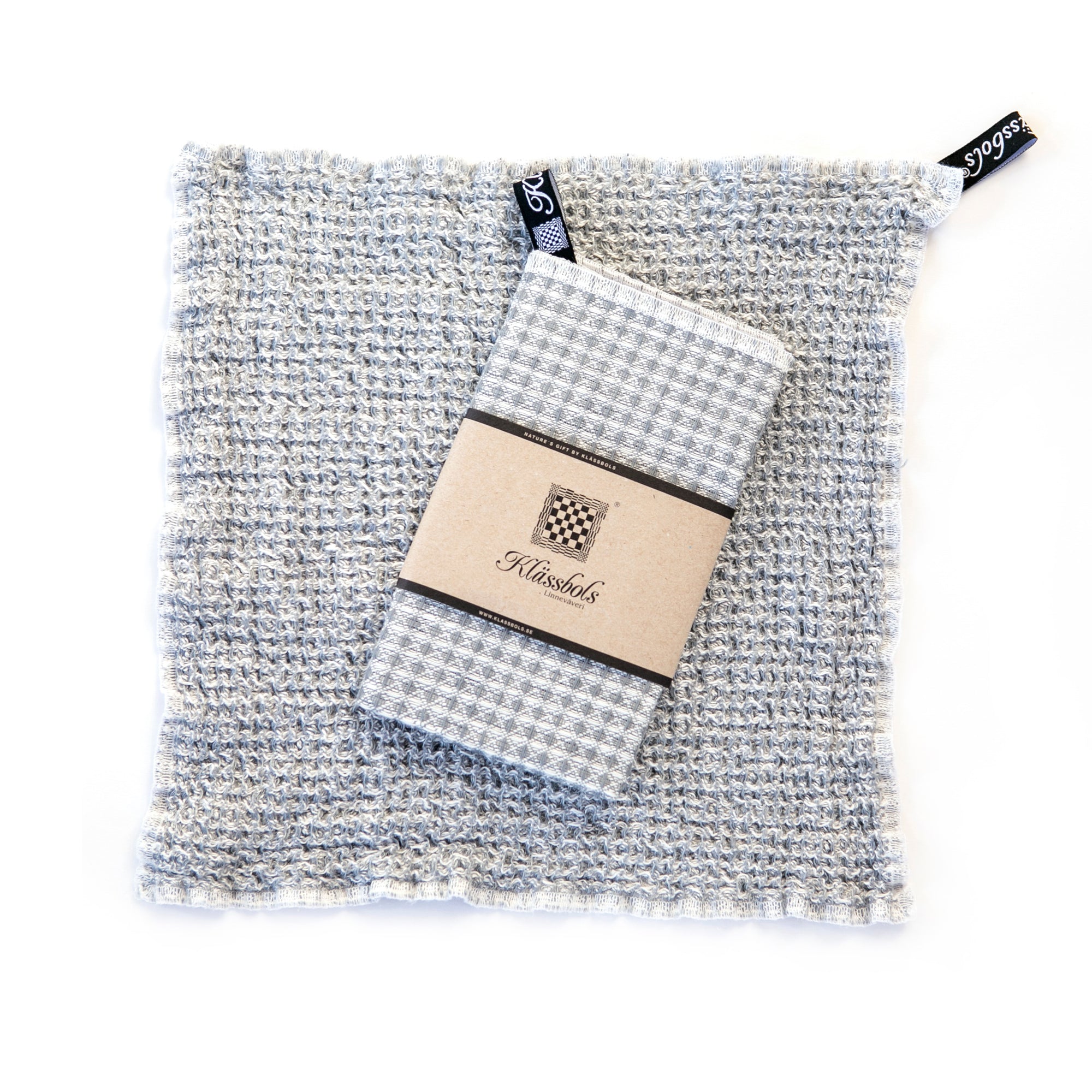 ein gewaschenes Spültuch Bubbel jeansblau Leinen Klässbols linneväveri Mys Shop mit einem neuen Spültuch mit Banderole obenauf liegend