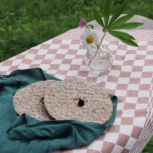 Ein kariertes Tischtuch aus Leinen in rose auf einem Tisch im Grünen, darauf ein kleines grünes Leinentuch mit schwedischem Knäckebrot