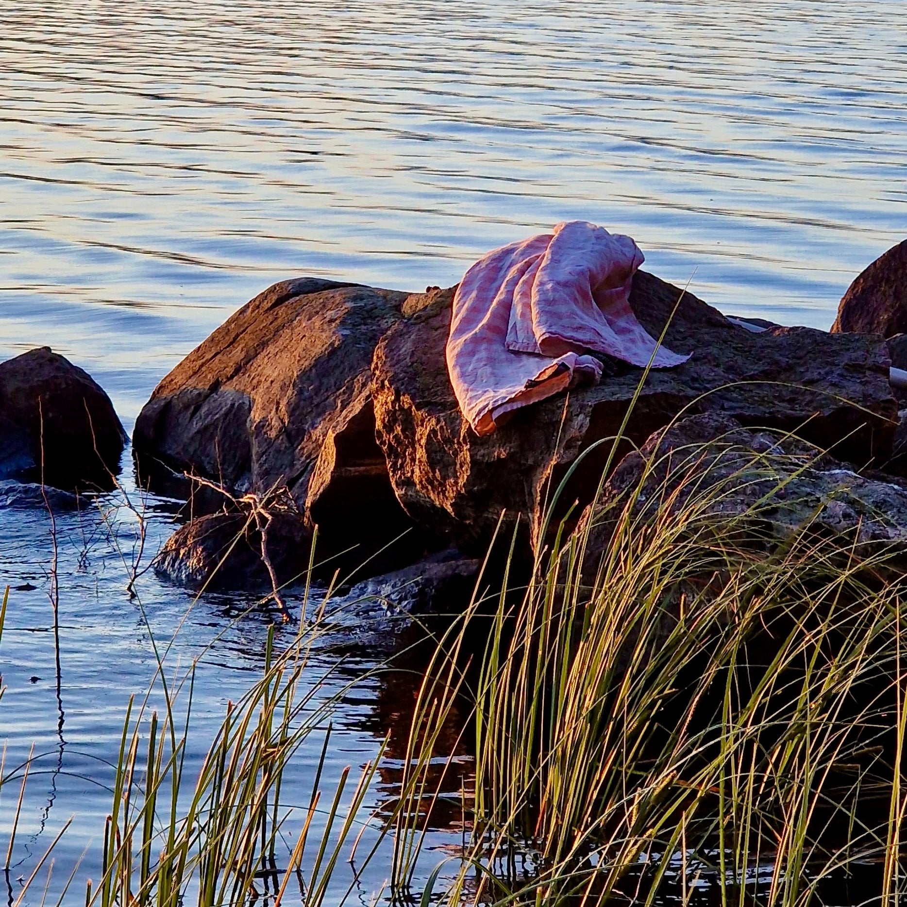Badetuch Regnbåge  aus Leinen in ziegelrot/sand bei Abendrot auf einem Stein im See