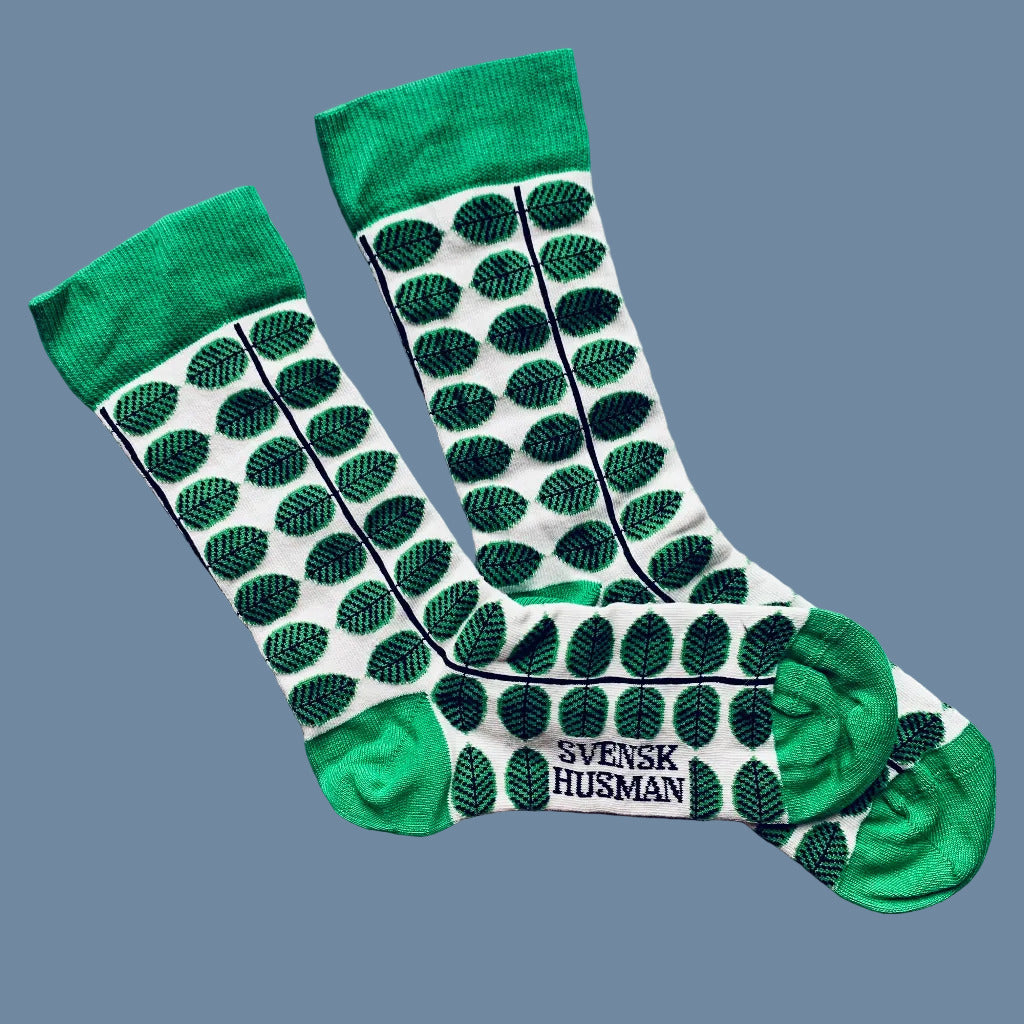 Weiße Socken mit grünen Blättern und grüner Ferse und Spitze nebeneinaderliegend vor mysblauem Hintergrund