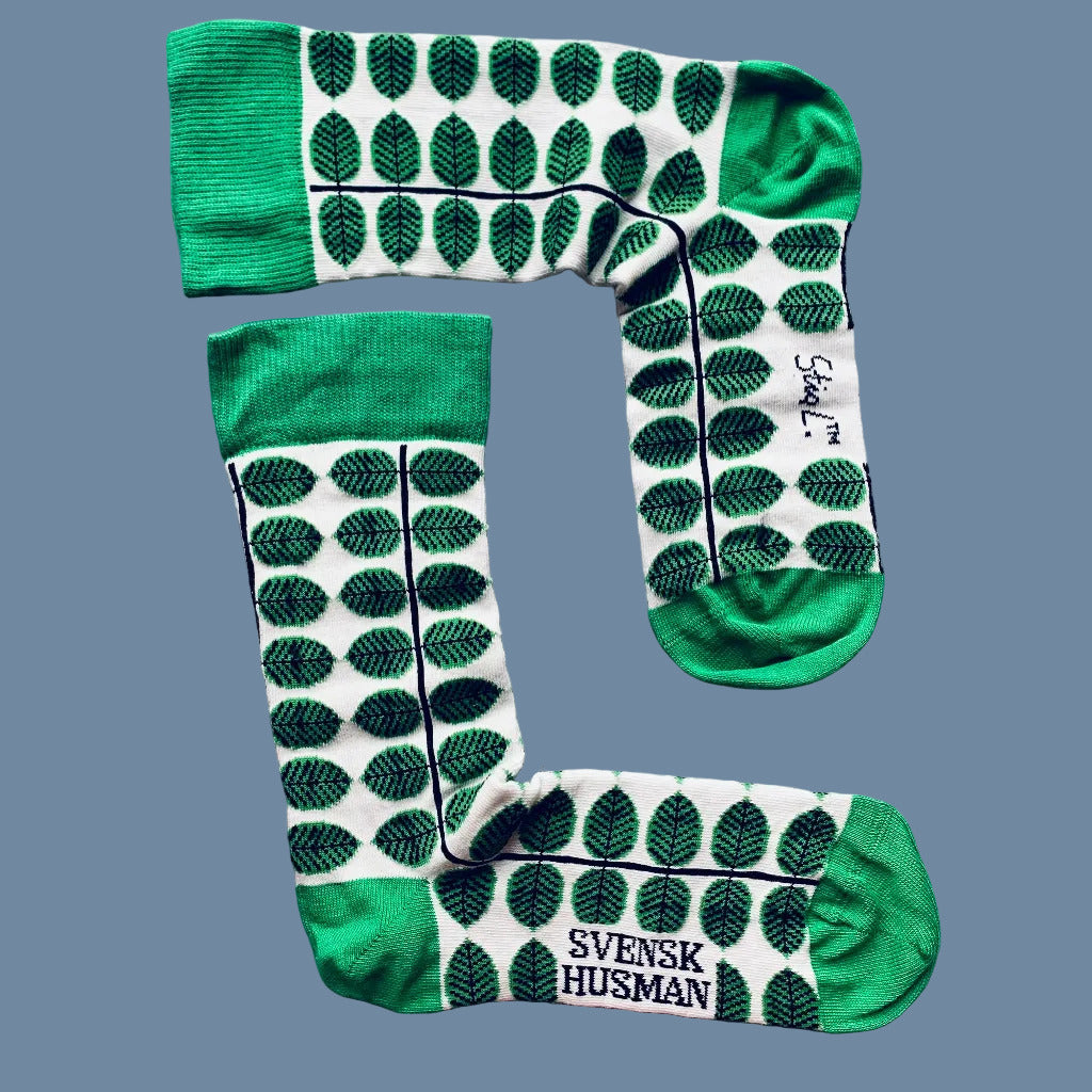 Weiße Socken mit grünen Blättern und grüner Ferse und Spitze vor mysblauem Hintergrund