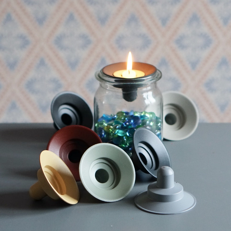 Kerzenständer Burk aus Metall auf Glas mit Glassteinen und brennender Kerze vor Schwedentapete
