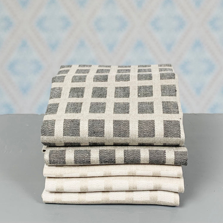 Handtuch aus Leinen Ruta natur und schwarz als Stapel vor Tapete im Laden