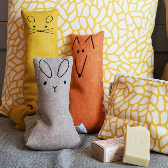 Hase, Fuchs uns Maus-Wärmekissen aus grauem, orangem bzw. gelbem Leinen stehen vor gelbem Kissen
