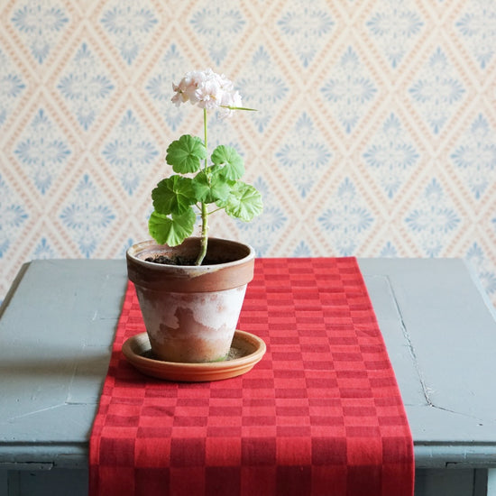 Tischläufer Karo in rot auf Tisch liegend mit Pelargonientopf