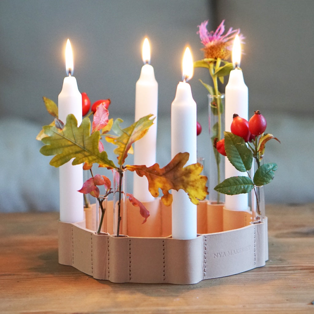 Kerzenhalter aus Leder mit vier brennenden Kerzen, dazwischen kleine Glasröhrchen mit Herbstlaub und Hagebutten