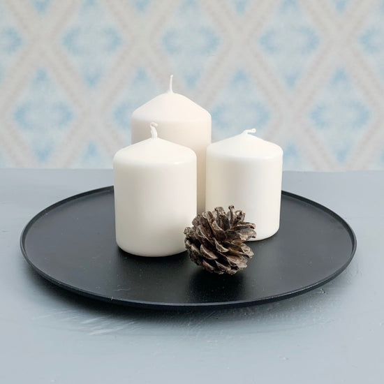 Kerzenteller Ljusfat Kerzenhalter für Blockkerzen Metall schwarz mit drei Blockkerzen und Kiefernzapfen auf Tisch