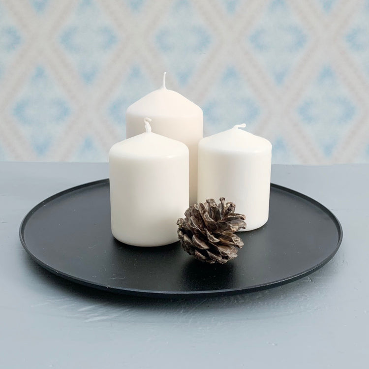 Kerzenteller Ljusfat Kerzenhalter für Blockkerzen Metall schwarz mit drei Blockkerzen und Kiefernzapfen auf Tisch