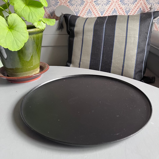 Kerzenteller Ljusfat schwarz in romantischem Setting auf Tisch mit Pelargonie und Leinenkissen im Hintergrund