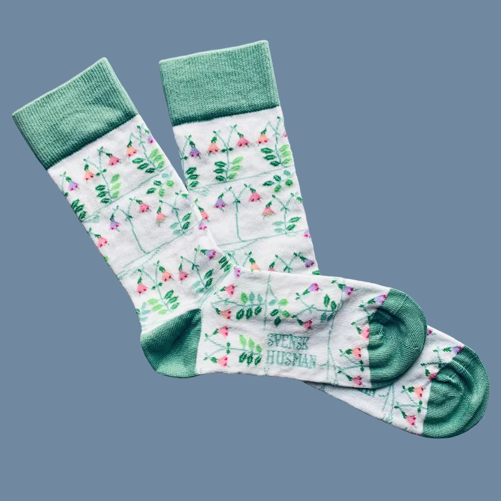 Weiße Socken mit Linnea Muster mit grüner Ferse und Spitze nebeneinanderliegend