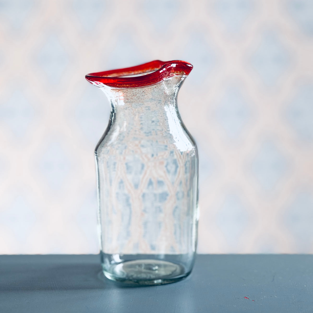 Milchkännchen aus Glas mit rotem Rand vor Schwedentapete