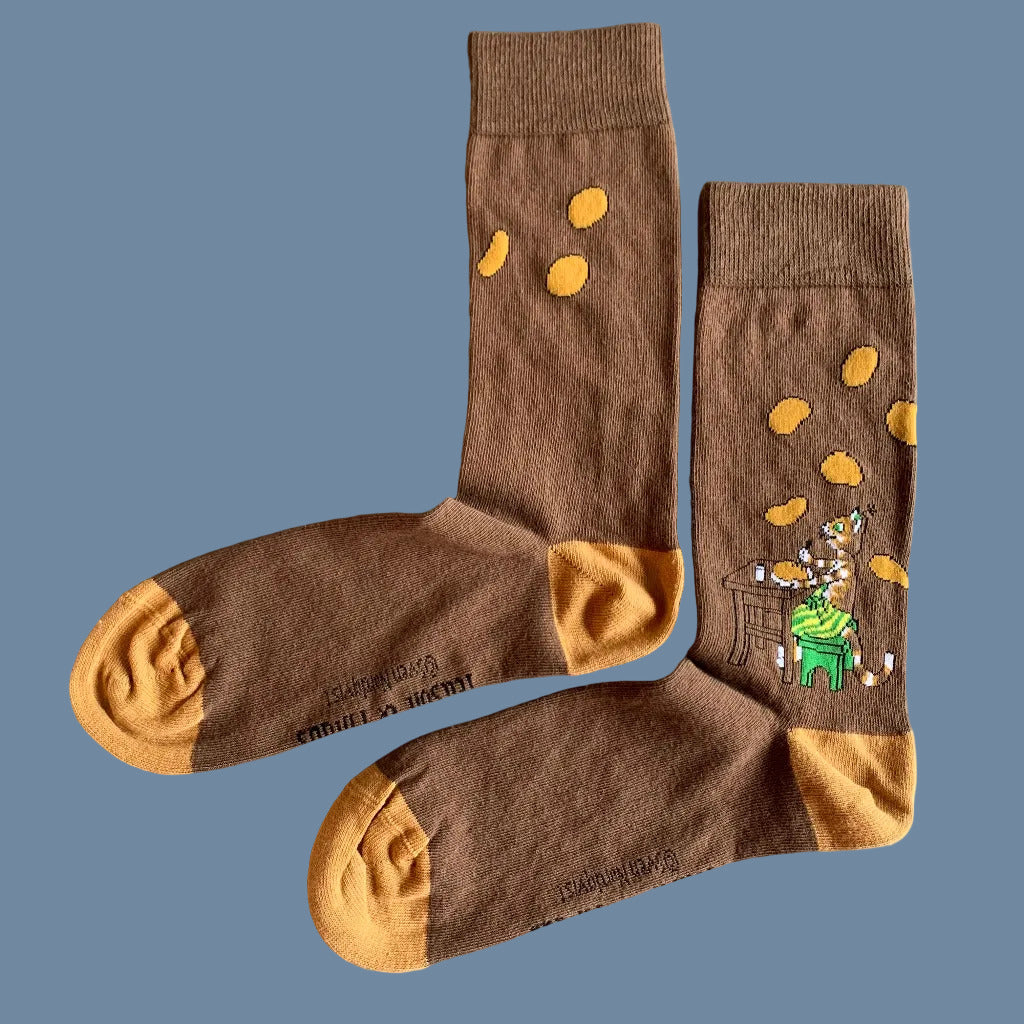 Braune Socken mit orangen Spitzen und Fersen und Findus am Tisch mit Pannkuchen