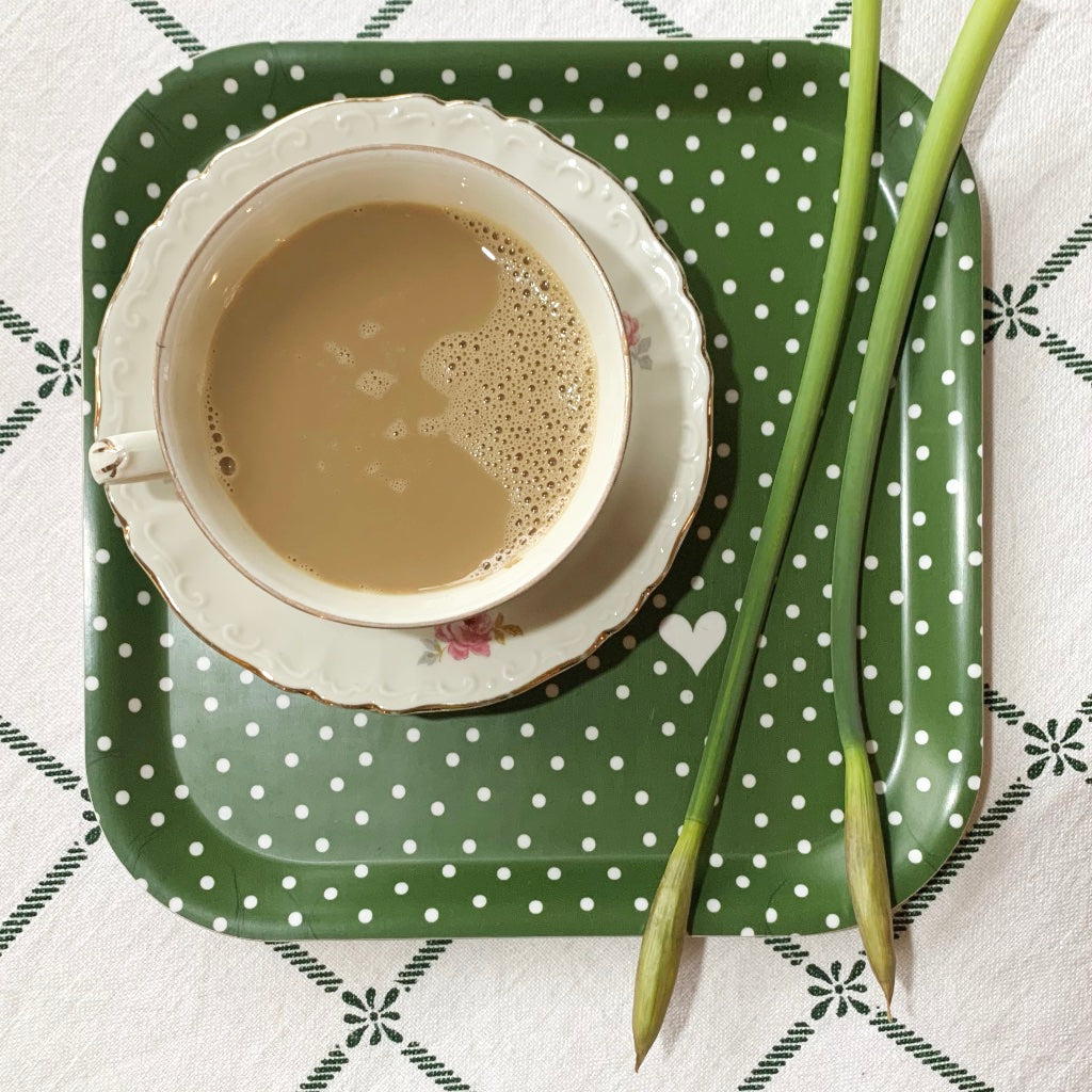 quadratisches Tablett in grün von oben mit Kaffeetasse und zwei Stengeln Osterglocken