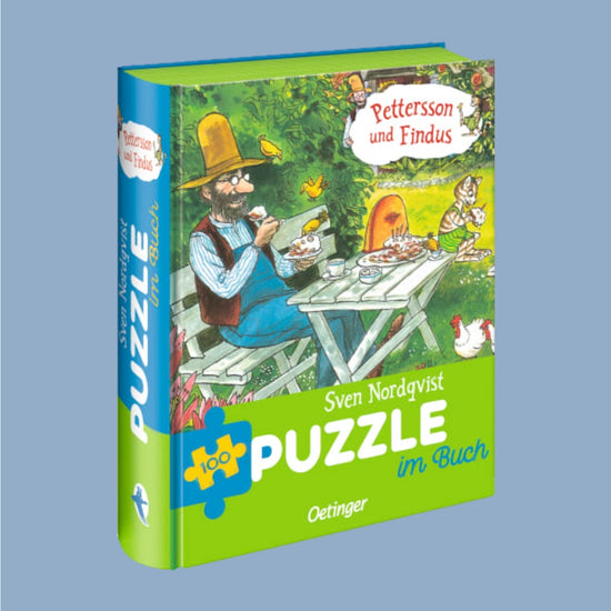 Ansicht des Puzzle-Buchs stehend mit blau grünem Rücken auf dem in weißen Großbuchstaben Puzzle steht, der Titel zeigt in den zwei oberen Dritteln das Puzzlebild (Pettersson und Findus sitzen im Garten und essen Pfannkuchentorte) und steht Puzzel im Buch