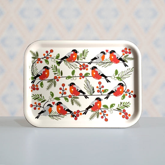 rechteckiges Holztablett mit Dompfaffen stehend vor Wand mt tyisch schwedischer Tapete