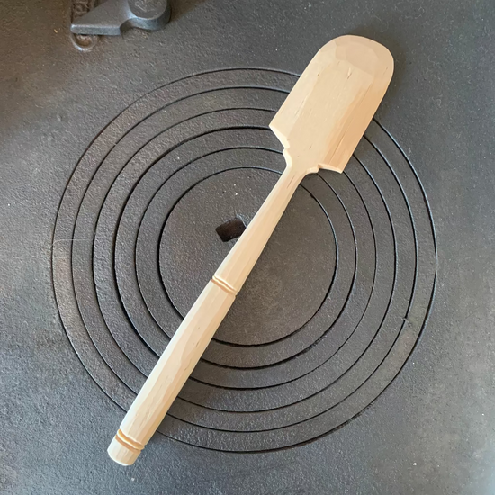 Handgeschnitzter Teigschaber aus Birkenholz in Natur mit Deko auf dem Stiel auf Küchenofen liegend