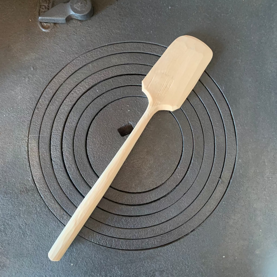 Handgeschnitzter Teigschaber aus Birkenholz in Natur auf Küchenofen liegend